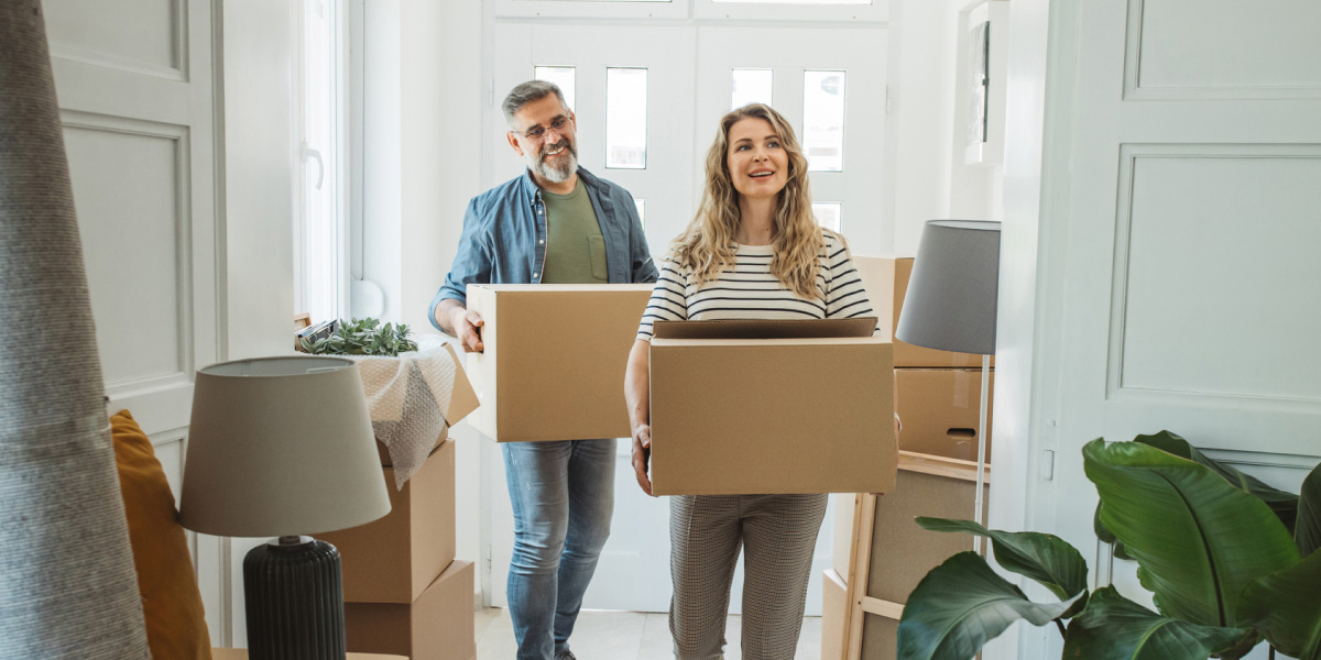 Man and woman carrying moving boxes into a bright home